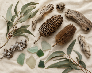 Flat lay of foraged natural materials on Driftwood Cream linen — eucalyptus leaves, banksia pods, sea glass, and driftwood
